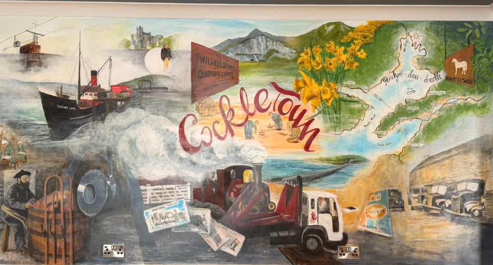 The Cockletown mural in the games room at Y Griffin: cockle-pickers on the estuary sands, the steam ship Florence Cooke, the Pwllheli Granite Company sign, a Ffestiniog steam engine, old delivery lorries and a hand-drawn map of Penrhyndeudraeth between its two beaches
